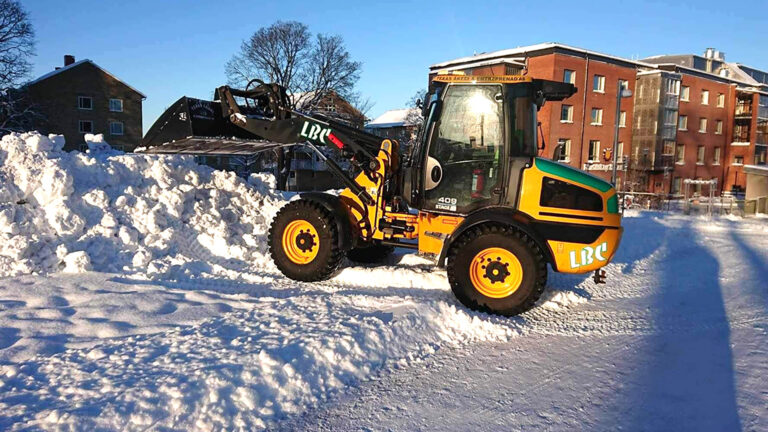 Bild på traktor-LBC Frakt som tippar snö på en snöhög i ett bostadsområde.