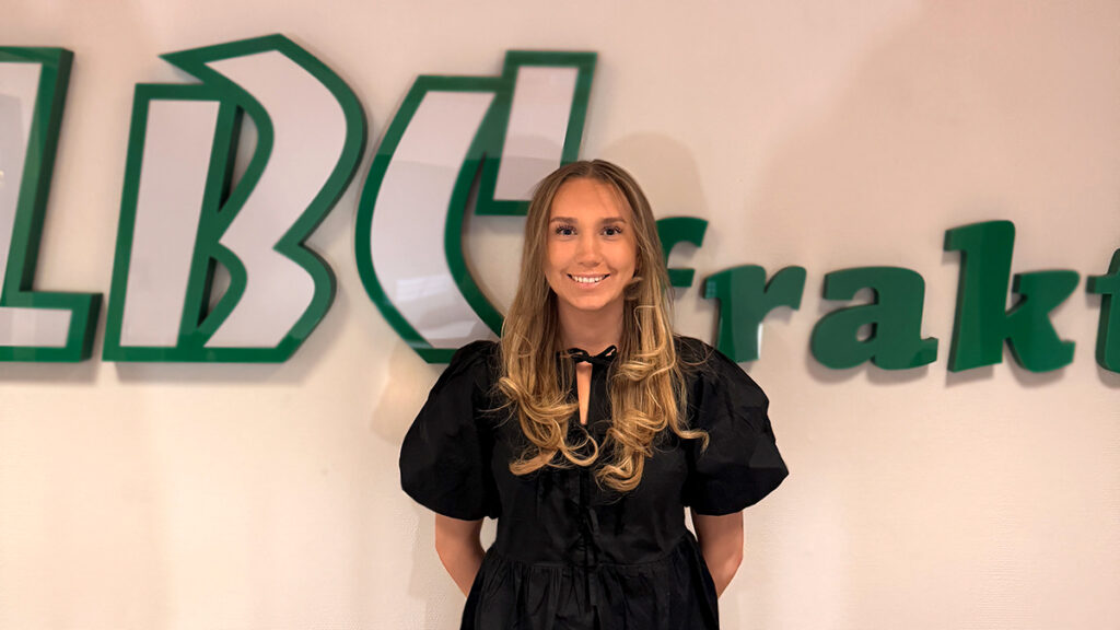 Porträtt på Karro Munk som står framför LBC Frakts logga.