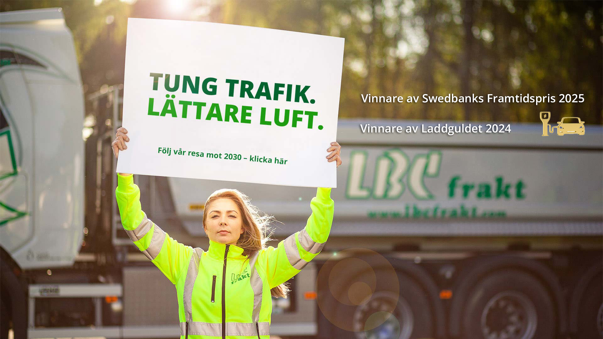 Bild på en kvinnlig chaufför som håller en skylt med texten: TUNG TRAFIK LÄTTARE LUFT Följ vår resa mot 2030- klicka här. Och texten: Vinnare av Swedbanks Framtidspris 2025Vinnare av Laddguldet 2024 + loggan för Laddguldet (en bil som laddar vid en stolpe. loggan är i guld).